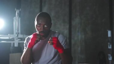Beden eğitiminde. Afrikalı dövüşçü boksörlere yumruk atmaya hazır koruyucu bandajları kameraya sarar. Güçlü bir adam boks antrenmanına hazırlanıyor.