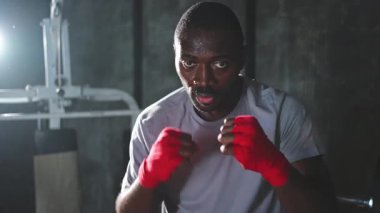 Beden eğitiminde. Afrikalı dövüşçü boksörlere yumruk atmaya hazır koruyucu bandajları kameraya sarar. Güçlü bir adam boks antrenmanına hazırlanıyor.