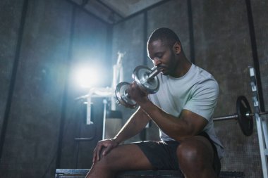 Beden eğitiminde spor. Spor salonunda dambılları toplayan Afrikalı Amerikalı bir vücut geliştirici. Fitness kulübünde halterli kasları çalıştırmak için ağırlık çalışıyorum. Spor yapan bir adam. Sağlıklı yaşam tarzı