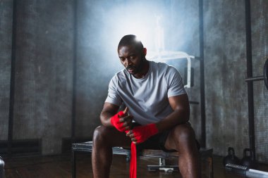 Beden eğitiminde spor. Afrikalı Amerikalı boksör elleri kırmızı boksla sarmalamaya hazırlanıyor spor amaçlı bandajlar spor salonunda. Güçlü adam boks antrenmanına hazır.
