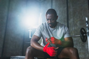 Beden eğitiminde spor. Afrikalı Amerikalı boksör elleri kırmızı boksla sarmalamaya hazırlanıyor spor amaçlı bandajlar spor salonunda. Güçlü adam boks antrenmanına hazır.