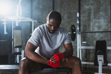 Beden eğitiminde spor. Afrikalı Amerikalı boksör elleri kırmızı boksla sarmalamaya hazırlanıyor spor amaçlı bandajlar spor salonunda. Güçlü adam boks antrenmanına hazır.