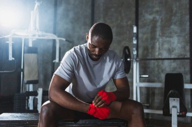 Beden eğitiminde spor. Afrikalı Amerikalı boksör elleri kırmızı boksla sarmalamaya hazırlanıyor spor amaçlı bandajlar spor salonunda. Güçlü adam boks antrenmanına hazır.
