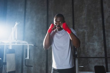Beden eğitiminde. Afrikalı dövüşçü boksörlere yumruk atmaya hazır koruyucu bandajları kameraya sarar. Güçlü bir adam boks antrenmanına hazırlanıyor.