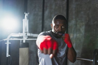 Beden eğitiminde. Afrikalı dövüşçü boksörlere yumruk atmaya hazır koruyucu bandajları kameraya sarar. Güçlü bir adam boks antrenmanına hazırlanıyor.