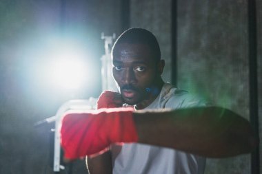 Beden eğitiminde. Afrikalı dövüşçü boksörlere yumruk atmaya hazır koruyucu bandajları kameraya sarar. Güçlü bir adam boks antrenmanına hazırlanıyor.