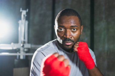Beden eğitiminde. Afrikalı dövüşçü boksörlere yumruk atmaya hazır koruyucu bandajları kameraya sarar. Güçlü bir adam boks antrenmanına hazırlanıyor.