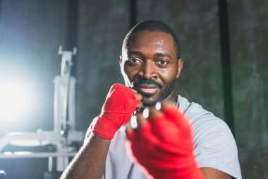 Beden eğitiminde. Afrikalı dövüşçü boksörlere yumruk atmaya hazır koruyucu bandajları kameraya sarar. Güçlü bir adam boks antrenmanına hazırlanıyor.
