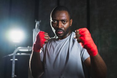 Spor salonunda boksör. Saldırgan Afrikalı dövüşçü boks eğitiminden sonra dinleniyor kameraya bakarak dövüşmeye hazır. Güçlü terli adam yumruklarını eğitiyor. Doğruca antrenmana hazırlanıyor.