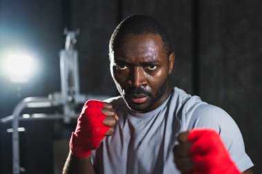 Spor salonunda boksör. Saldırgan Afrikalı dövüşçü boks eğitiminden sonra dinleniyor kameraya bakarak dövüşmeye hazır. Güçlü terli adam yumruklarını eğitiyor. Doğruca antrenmana hazırlanıyor.