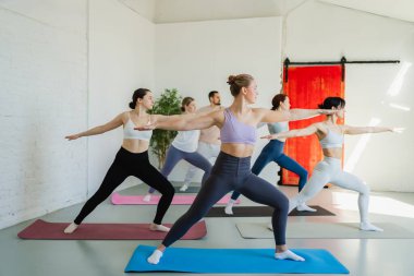 Yoga sınıfı pilates egzersizi. Bir grup sporcu, yoga sağIık meditasyonu için stüdyo sınıfında egzersiz yapıyor. Spor salonunda yoga yapan erkek antrenörler. Spor salonunda esneme hareketleri yapan kadınlar.