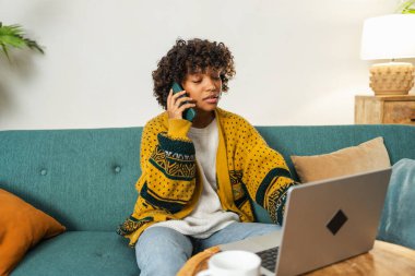 Afro-Amerikalı kadın ofis telefonunda dizüstü bilgisayar kullanıyor. Mutlu iş kızı sanal toplantı yapıyor. İçerde çalışan bir kadın iletişim için bilgisayarını kullanıyor. Uzak çalışma