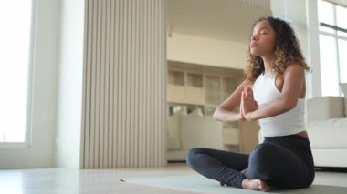 Yoga farkındalığı meditasyonu. Genç sağlıklı Afrikalı kız evde yoga yapıyor. Lotus 'ta oturan kadın yoga minderinde poz veriyor içeride meditasyon yapıyor. Nefes egzersizi yapan bir kız. Evde yoga.