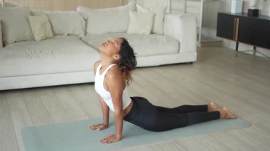 Yoga fitness antrenmanı. Sağlıklı Afrikalı kız evde yoga yapıyor. Pilates antrenmanı yapan bir kadın, yoga minderiyle spor yapıyor. Kız kilo vermek için antrenman yapıyor. Spor uygunluğu