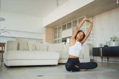 Yoga fitness antrenmanı. Sağlıklı Afrikalı kız evde yoga yapıyor. Pilates antrenmanı yapan bir kadın, yoga minderiyle spor yapıyor. Kız kilo vermek için antrenman yapıyor. Spor uygunluğu