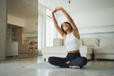 Yoga fitness antrenmanı. Sağlıklı Afrikalı kız evde yoga yapıyor. Pilates antrenmanı yapan bir kadın, yoga minderiyle spor yapıyor. Kız kilo vermek için antrenman yapıyor. Spor uygunluğu