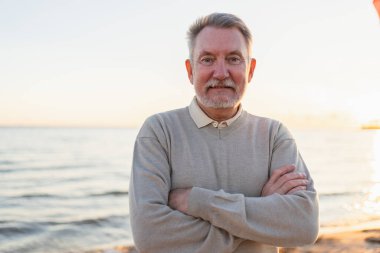 Sahilde kendine güveni tam orta yaşlı bir Avrupalı 'nın açık hava portresi. Yaşlı, olgun bir adam gülümsüyor. Mutlu büyükbaba kameraya bakıyor. Yüz portresi yakın çekim. Mutlu insanlar.