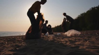 Dünya günü. Gönüllü eylemciler sahil bölgesindeki çöpleri topluyor. Kadınlar ve erkekler okyanus kıyısındaki çöp torbasına plastik çöp koyar. Çevre koruma kıyı bölgesi temizliği
