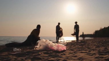 Dünya günü. Gönüllü eylemciler sahil bölgesindeki çöpleri topluyor. Kadınlar ve erkekler okyanus kıyısındaki çöp torbasına plastik çöp koyar. Çevre koruma kıyı bölgesi temizliği