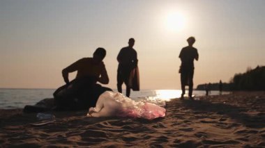 Dünya günü. Gönüllü eylemciler sahil bölgesindeki çöpleri topluyor. Kadınlar ve erkekler okyanus kıyısındaki çöp torbasına plastik çöp koyar. Çevre koruma kıyı bölgesi temizliği