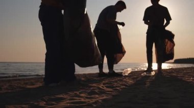 Dünya günü. Gönüllü eylemciler sahil bölgesindeki çöpleri topluyor. Kadınlar ve erkekler okyanus kıyısındaki çöp torbasına plastik çöp koyar. Çevre koruma kıyı bölgesi temizliği