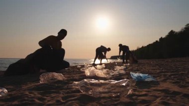 Dünya günü. Gönüllü eylemciler sahil bölgesindeki çöpleri topluyor. Kadınlar ve erkekler okyanus kıyısındaki çöp torbasına plastik çöp koyar. Çevre koruma kıyı bölgesi temizliği