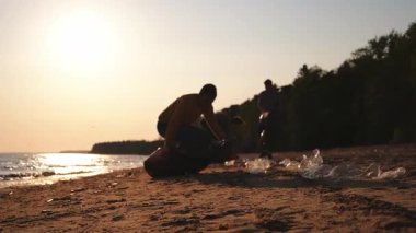Dünya günü. Gönüllü eylemciler sahil bölgesindeki çöpleri topluyor. Kadınlar ve erkekler okyanus kıyısındaki çöp torbasına plastik çöp koyar. Çevre koruma kıyı bölgesi temizliği
