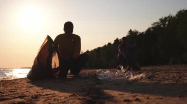 Dünya günü. Gönüllü eylemciler sahil bölgesindeki çöpleri topluyor. Kadınlar ve erkekler okyanus kıyısındaki çöp torbasına plastik çöp koyar. Çevre koruma kıyı bölgesi temizliği