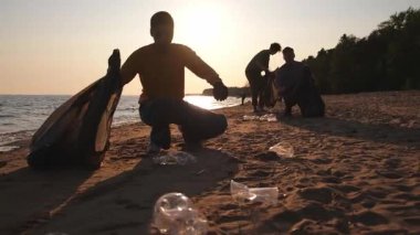 Dünya günü. Gönüllü eylemciler sahil bölgesindeki çöpleri topluyor. Kadınlar ve erkekler okyanus kıyısındaki çöp torbasına plastik çöp koyar. Çevre koruma kıyı bölgesi temizliği