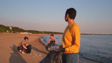 Dünya günü. Gönüllü eylemciler, sahil bölgesindeki çöpleri topluyor. Kadın, okyanus kıyısındaki çöp poşetine plastik şişe koyuyor. Çevre koruma kıyı bölgesi temizliği