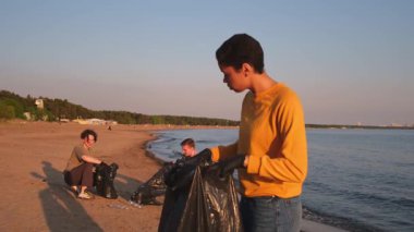 Dünya günü. Gönüllü eylemciler, sahil bölgesindeki çöpleri topluyor. Kadın, okyanus kıyısındaki çöp poşetine plastik şişe koyuyor. Çevre koruma kıyı bölgesi temizliği