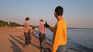Dünya günü. Gönüllü eylemciler, sahil bölgesindeki çöpleri topluyor. Kadın, okyanus kıyısındaki çöp poşetine plastik şişe koyuyor. Çevre koruma kıyı bölgesi temizliği