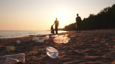 Dünya günü. Gönüllü eylemciler sahil bölgesindeki çöpleri topluyor. Kadınlar ve erkekler okyanus kıyısındaki çöp torbasına plastik çöp koyar. Çevre koruma kıyı bölgesi temizliği