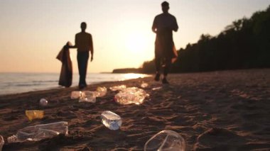 Dünya günü. Gönüllü eylemciler sahil bölgesindeki çöpleri topluyor. Kadınlar ve erkekler okyanus kıyısındaki çöp torbasına plastik çöp koyar. Çevre koruma kıyı bölgesi temizliği