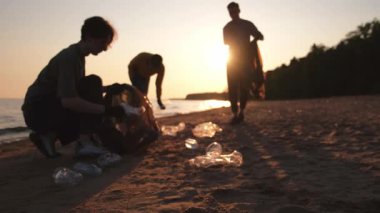 Dünya günü. Gönüllü eylemciler sahil bölgesindeki çöpleri topluyor. Kadınlar ve erkekler okyanus kıyısındaki çöp torbasına plastik çöp koyar. Çevre koruma kıyı bölgesi temizliği