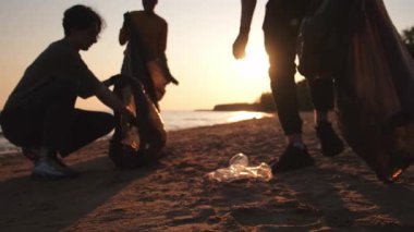 Dünya günü. Gönüllü eylemciler sahil bölgesindeki çöpleri topluyor. Kadınlar ve erkekler okyanus kıyısındaki çöp torbasına plastik çöp koyar. Çevre koruma kıyı bölgesi temizliği