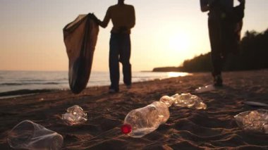 Dünya günü. Gönüllü eylemciler sahil bölgesindeki çöpleri topluyor. Kadınlar ve erkekler okyanus kıyısındaki çöp torbasına plastik çöp koyar. Çevre koruma kıyı bölgesi temizliği
