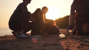 Dünya günü. Gönüllü eylemciler sahil bölgesindeki çöpleri topluyor. Kadınlar ve erkekler okyanus kıyısındaki çöp torbasına plastik çöp koyar. Çevre koruma kıyı bölgesi temizliği