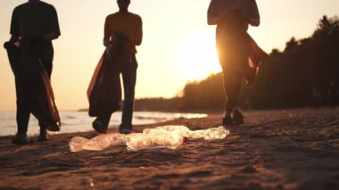 Dünya günü. Gönüllü eylemciler sahil bölgesindeki çöpleri topluyor. Kadınlar ve erkekler okyanus kıyısındaki çöp torbasına plastik çöp koyar. Çevre koruma kıyı bölgesi temizliği