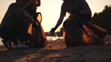 Dünya günü. Gönüllü eylemciler sahil bölgesindeki çöpleri topluyor. Kadınlar ve erkekler okyanus kıyısındaki çöp torbasına plastik çöp koyar. Çevre koruma kıyı bölgesi temizliği
