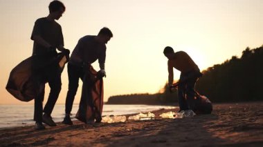 Dünya günü. Gönüllü eylemciler sahil bölgesindeki çöpleri topluyor. Kadınlar ve erkekler okyanus kıyısındaki çöp torbasına plastik çöp koyar. Çevre koruma kıyı bölgesi temizliği