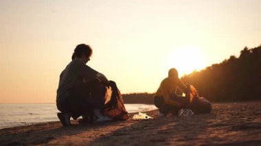 Dünya günü. Gönüllü eylemciler sahil bölgesindeki çöpleri topluyor. Kadınlar ve erkekler okyanus kıyısındaki çöp torbasına plastik çöp koyar. Çevre koruma kıyı bölgesi temizliği