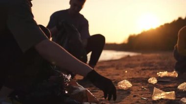 Dünya günü. Gönüllü eylemciler sahil bölgesindeki çöpleri topluyor. Kadınlar ve erkekler okyanus kıyısındaki çöp torbasına plastik çöp koyar. Çevre koruma kıyı bölgesi temizliği