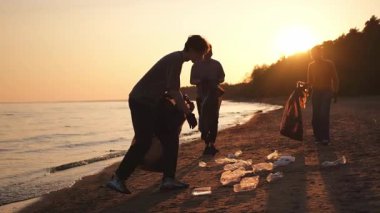 Dünya günü. Gönüllü eylemciler sahil bölgesindeki çöpleri topluyor. Kadınlar ve erkekler okyanus kıyısındaki çöp torbasına plastik çöp koyar. Çevre koruma kıyı bölgesi temizliği