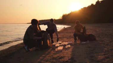 Dünya günü. Gönüllü eylemciler sahil bölgesindeki çöpleri topluyor. Kadınlar ve erkekler okyanus kıyısındaki çöp torbasına plastik çöp koyar. Çevre koruma kıyı bölgesi temizliği