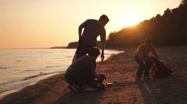 Dünya günü. Gönüllü eylemciler sahil bölgesindeki çöpleri topluyor. Kadınlar ve erkekler okyanus kıyısındaki çöp torbasına plastik çöp koyar. Çevre koruma kıyı bölgesi temizliği