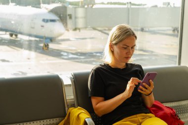 Havaalanı terminali. Akıllı telefon kullanan bir kadın uçuşu bekliyor. Havaalanında cep telefonlu bir kız internet sosyal medya uygulamalarında sörf yapıyor. Havayolu merkezinin pansiyonunda seyahat eden bir kadın. Gezgin kız.