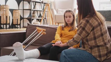 Kırık bacağı alçıda olan bir kız evde kanepede annesiyle oturuyor. Kırık bacağı iyileşen üzgün genç bir çocuk. Hızlı rehabilitasyon için koltuk değneklerini kullanan bir kız. Anne destek kızı