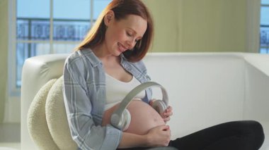 Hamilelik anneliği. Karnının yanında kulaklık tutan hamile bir kadın anne ve doğmamış bebek için müzik dinliyor. Hamilelikten zevk alan bir kız sakin olmak için müzik dinler. Doğum öncesi müzik uyarımı