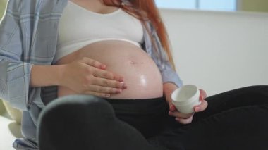 Hamilelik anneliği. Koca göbeğine krem süren hamile bir kadın cildine iyi gelir. Gerilme izinin önlenmesi için kozmetik ürün. Evde hamileliğin tadını çıkaran bir kız. Annelik sağlığı kavramı